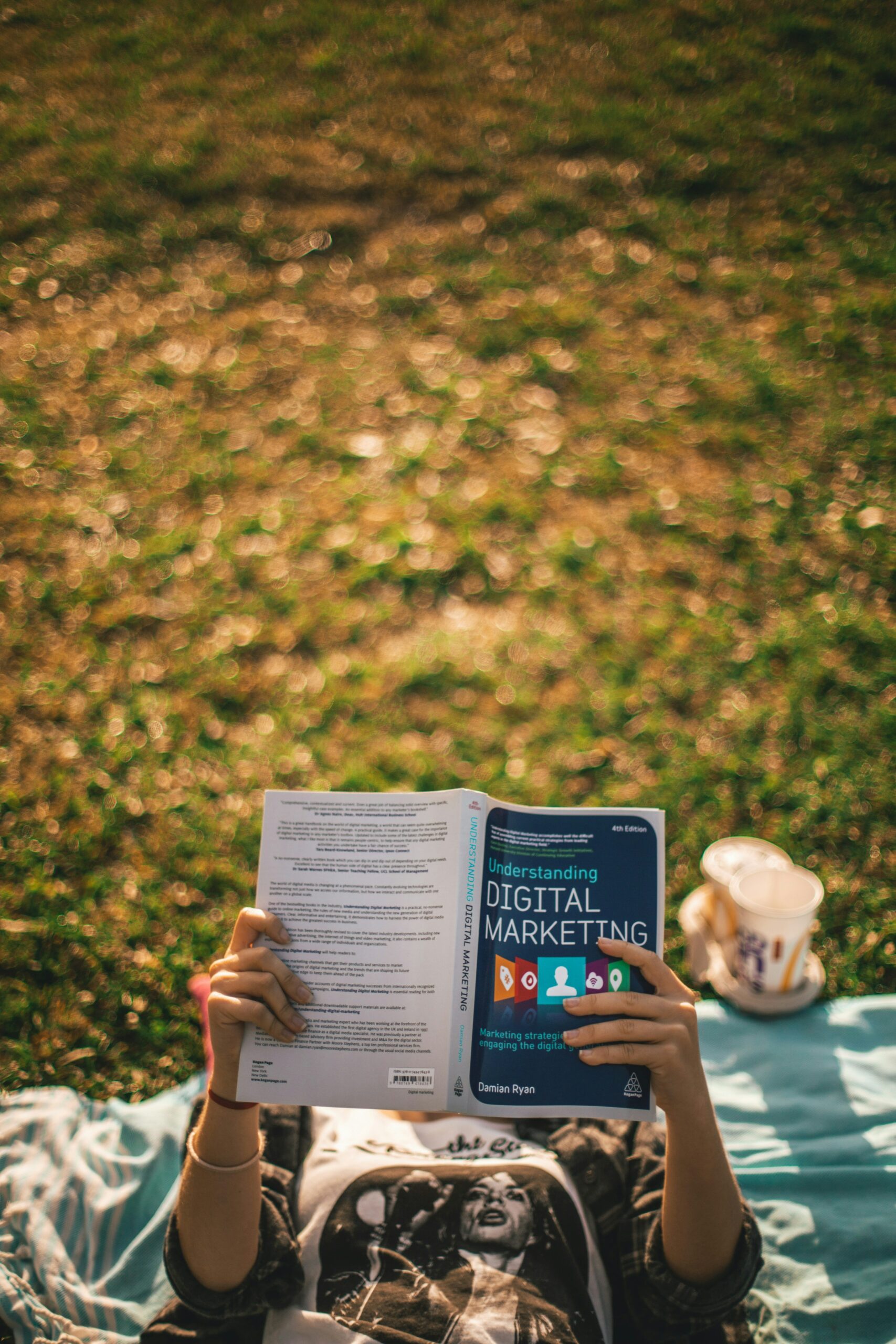 What is Digital PR? 1 Digital PR - A person lies on a blanket in the grass, reading "Understanding Digital Marketing and Digital PR" A drink in a cup is beside them.
